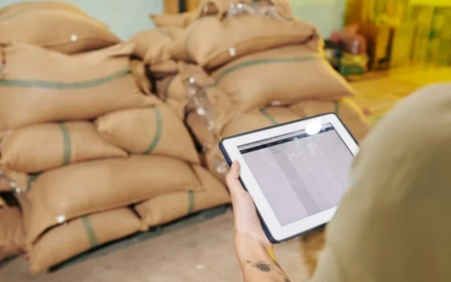 Technician recording pest control checks on a tablet beside stacked grain sacks