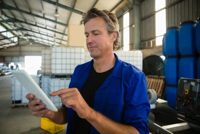 Technician in blue overalls using a tablet beside industrial chemical storage containers
