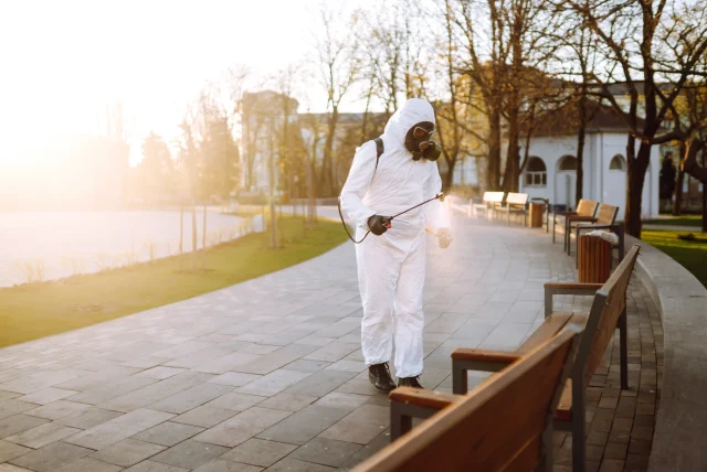 Pest control technician in protective coveralls treating the exterior grounds of a commercial property